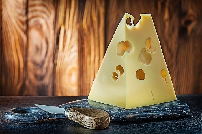 Maasdam cheese big piece and knife on little curving board old wooden background, by Dzmitri Mikhaltsow