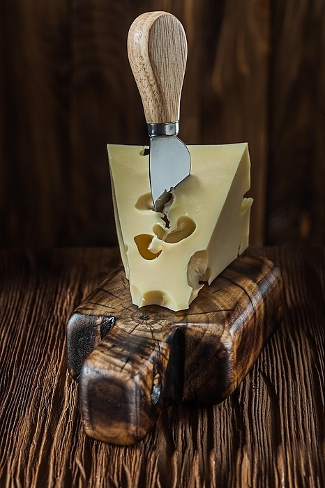 Maasdam cheese on vintage cutting board and knife old dark wooden background, by Dzmitri Mikhaltsow