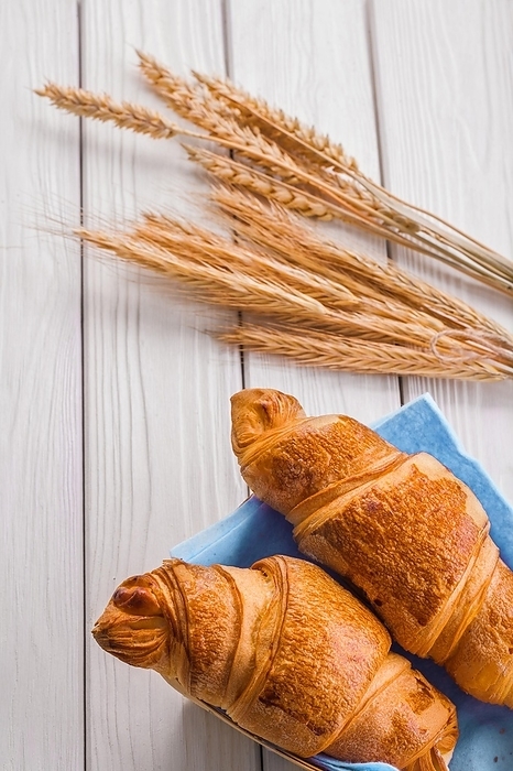 Croissants and ears of wheat on white wooden boards, by Dzmitri Mikhaltsow