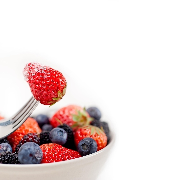 Srawberry on a fork with sugar crust and bowl of mixed berries on white background, by keko64