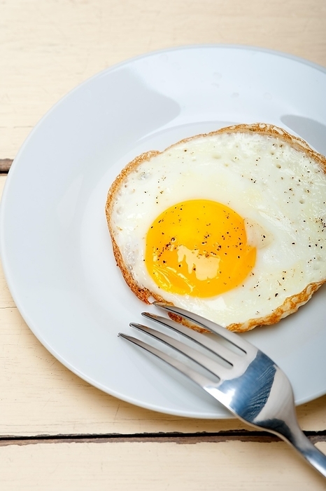 Fried egg sunny side up on a plate with fork over wood table, by Fracesco Perre