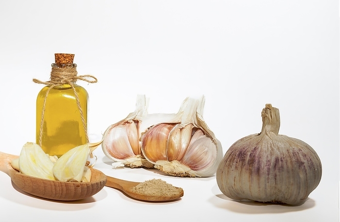 Whole, powdered and chopped garlic on a white background with a glass bottle with olive oil, by jose hernandez antona