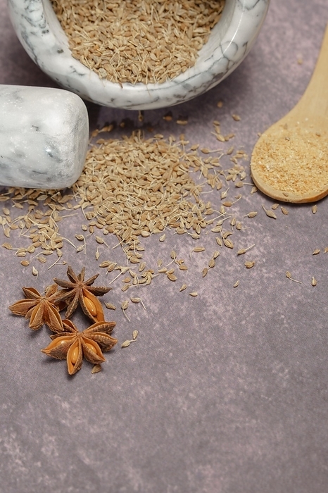 Whole dried anise (Pimpinella anisum) seeds in a ceramic mortar and pestle, with ground anise and star anise, by joseantona