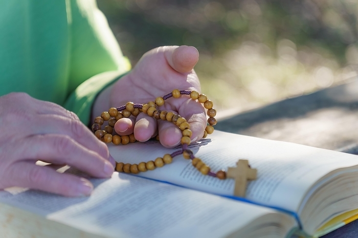 A woman's hands praying the rosary in the field over an open bible on a wooden table, by joseantona