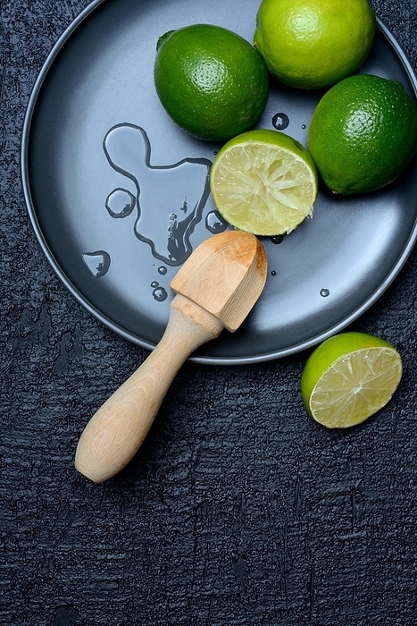 Limes with citrus squeezer on plate, halved, by Jürgen Pfeiffer