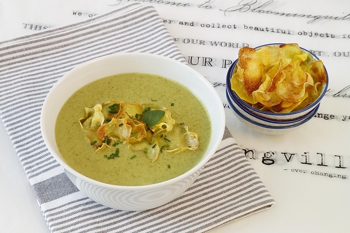 Swabian cuisine, cress soup with crisps, cress, plate with green cream soup, soup bowl, garnished with herbs, hearty soup, bowl with crisps, tea towel, writing, letters, vegetarian, healthy, salty, cooking, typical Swabian reinterpreted, traditional cuisine, food photography, studio, tablecloth, Germany, Europe, by Katharina Hild