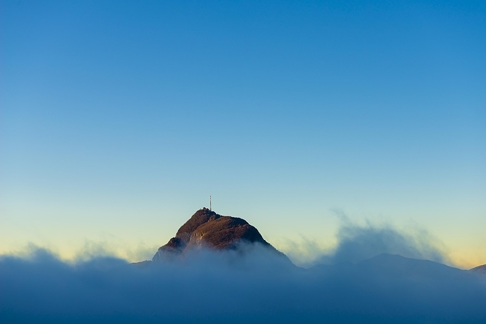 Mountain Peak San Salvatore Above Cloudscape with Sunlight and Clear Sky in Lugano, Ticino in Switzerland, by Mats Silvan