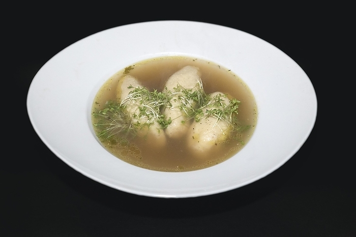 Three semolina dumplings swimming in a beef broth in a white porcelain plate, garnished with cress, typical Austrian speciality, food photography with black background, by Siegra Asmoel