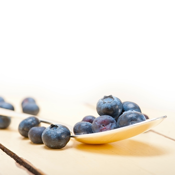 Fresh blueberry on silver spoon over a white rustic wood table, by Francesco Perre