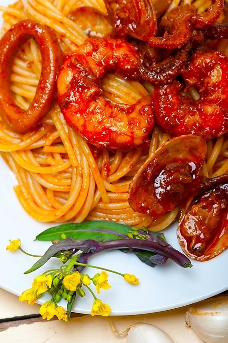 Italian seafood spaghetti pasta on red tomato sauce over white rustic wood table, by Francesco Perre