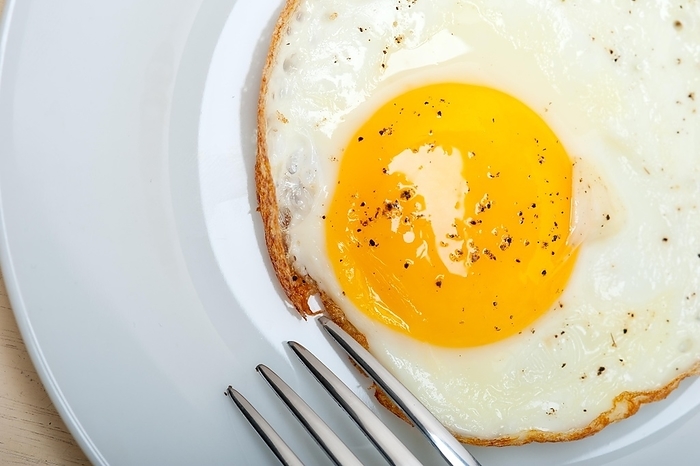 Fried egg sunny side up on a plate with fork over wood table, by Fracesco Perre