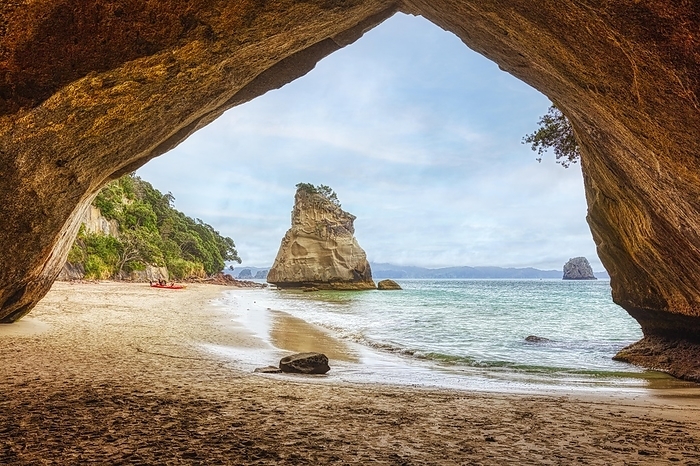 View from a cave onto a beach and isolated rocks in the sea, under a cloudy sky, Cathedral Grove, Coromandel, New Zealand, Oceania, by Norbert Achtelik