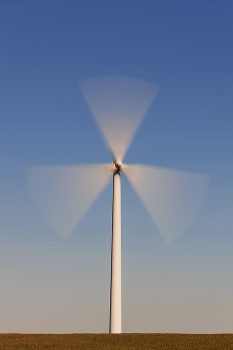 Spinning blades of windturbine in field against blue sky, by alimdi / Arterra