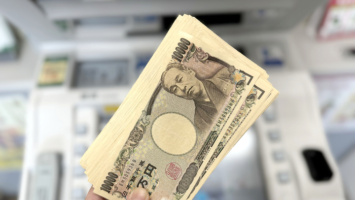 Lots of 10,000 yen bills held in front of ATM_wide