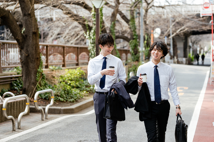 Two shirtless Japanese businessmen in business suits walking side by side on the greenway, smiling and conversing (People)