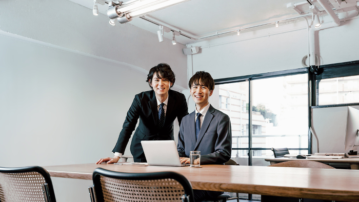 Two Japanese men, co-owners of a small business and a startup, smiling and looking at the camera with confident expressions on their faces at an office conference table (People)
