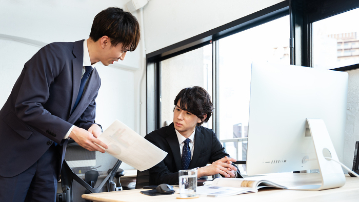 A Japanese man in his thirties in a managerial position, seriously reporting and consulting with his subordinates (People)