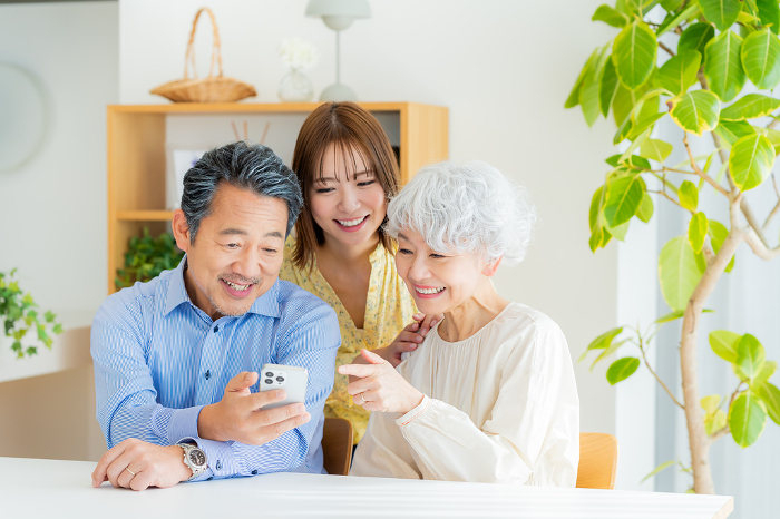 Japanese senior couple and their child looking at a smartphone in the living room (People)