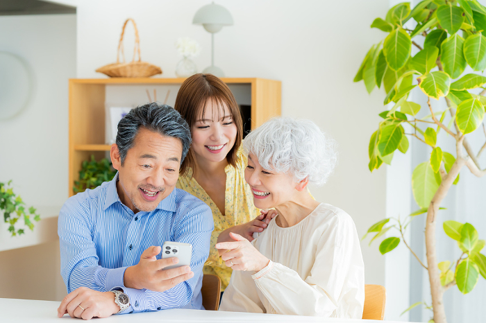 Japanese senior couple and their child looking at a smartphone in the living room (People)