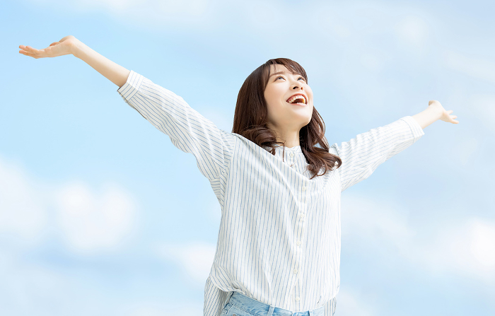 Smiling Japanese woman holding her arms out to the blue sky (People)