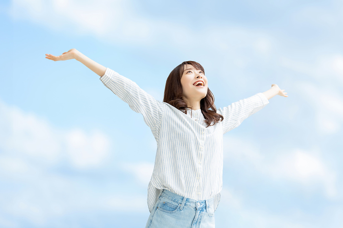 Smiling Japanese woman holding her arms out to the blue sky (People)