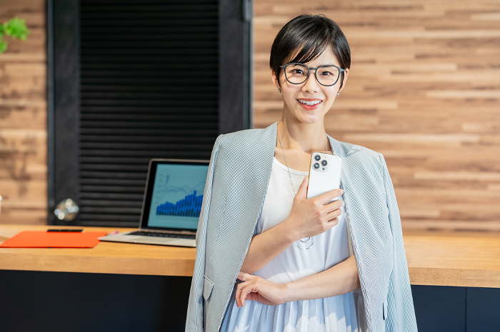 Japanese businesswoman holding a smartphone in her office （Female / People)