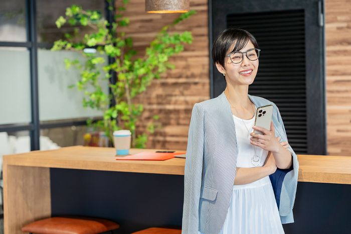 Japanese businesswoman holding a smartphone in her office （Female / People)