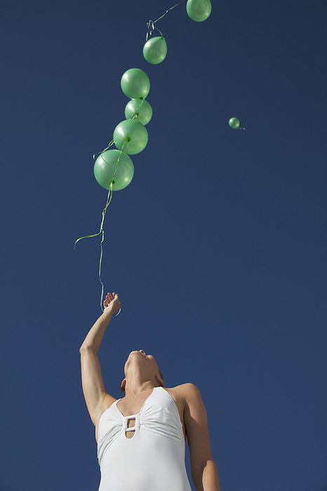 Woman releasing green balloons in a cloudless sky - low angle view