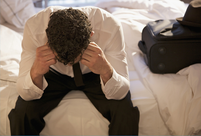 Businessman sitting on a bed with his head in his hands