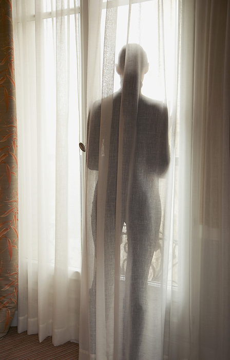 Silhouette of a woman behind a semi transparent curtain, back view