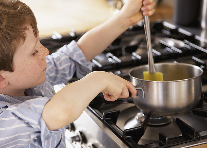 Young boy stirring and holding a saucepan over a cooker