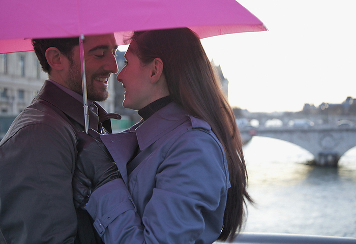 Close up of a couple hugging under a pink umbrella by the Seine river, Paris, France