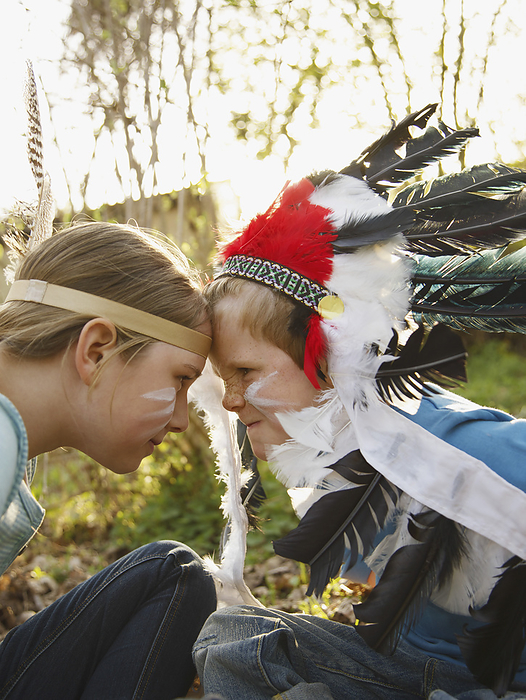 Boy and girl wearing indian feather headdresses sitting face to face