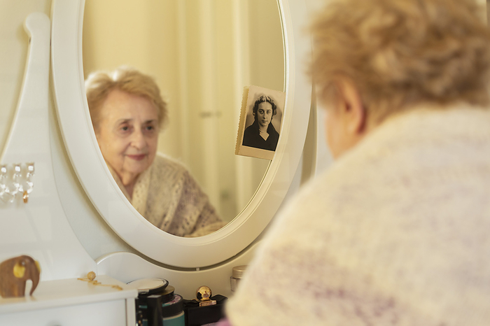 Smiling senior woman looking at reflection in mirror next to old photograph
