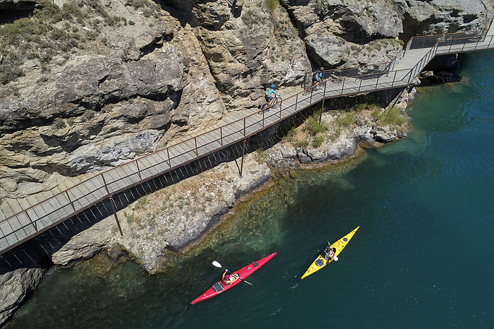 New Zealand Cyclists on cantilever bridge on Lake Dunstan Cycle Trail, and kayakers, Lake Dunstan, near Cromwell, Central Otago, South Island, New Zealand   drone aerial