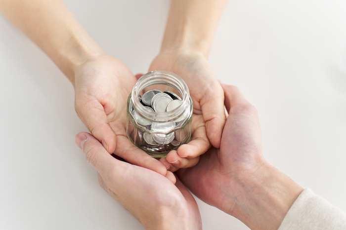 Hands of a man and a woman placing a jar containing coins