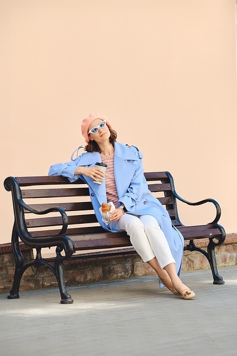 Careless woman in coral beret and blouse, blue raincoat and sunglasses sitting on bench with snack, by Aleksei Isachenko
