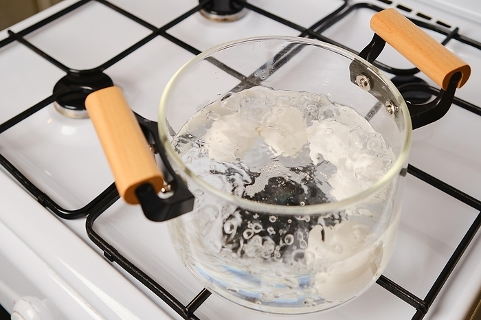 Overhead view of transparent glass saucepan with boiling eggs on a gas stove, by Aleksei Isachenko