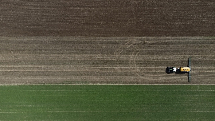 A green tractor with a yellow slurry tanker fertilises a harvested field, bird's eye view, drone shot, Lower Bavaria, Bavaria, Germany, Europe, by Gerhard Nixdorf