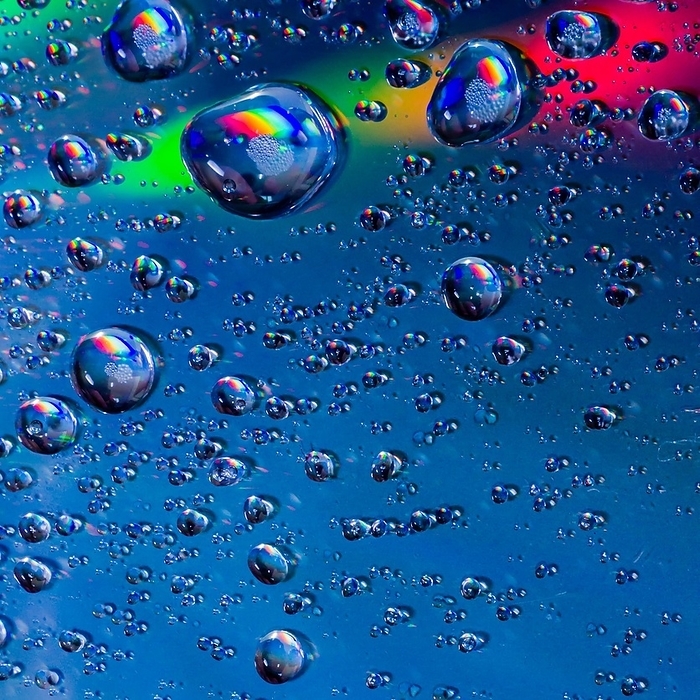 Closeup of water drops on a blue field with rainbow colors cutting across top of image, by John Erskin