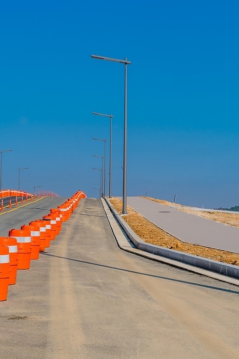Street lights traffic barrels lining newly constructed road next to vacant land at construction site under clear blue sky, South Korea, South Korea, Asia, by aminkorea
