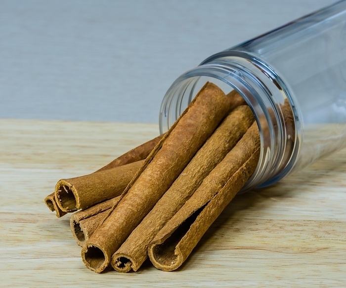 Cinnamon sticks extending out of a glass jar on a wooded cutting board, by aminkorea