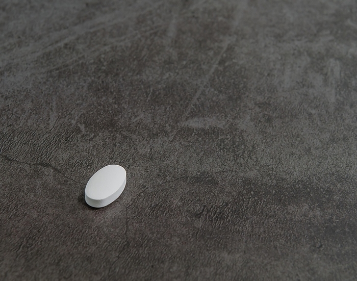 Closeup of one white coral calcium vitamin tablet isolated on black textured background, by aminkorea