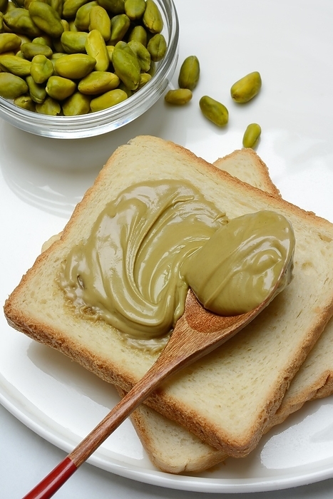 Pistachio cream with a spoon on slices of bread, pistachio in small bowls, by Jürgen Pfeiffer