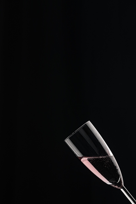 A champagne glass filled with rosé sparkling wine against a black background, by Lucas Seebacher