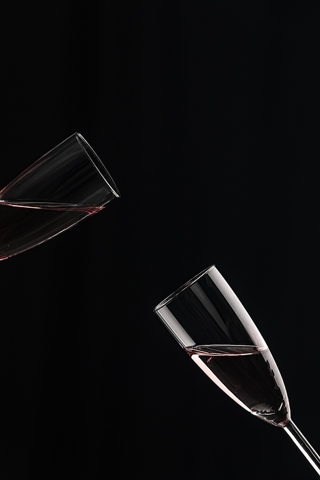 Two half-filled champagne glasses tilted towards each other against a black background, by Lucas Seebacher