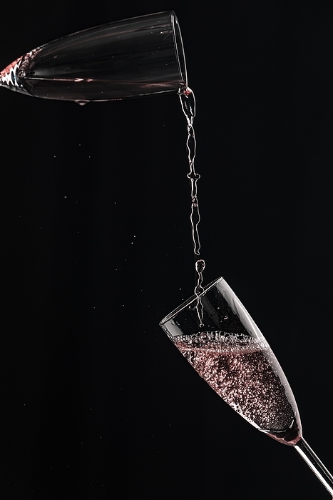 Rosé champagne flows from one champagne glass into another, captured in motion, black background, by Lucas Seebacher