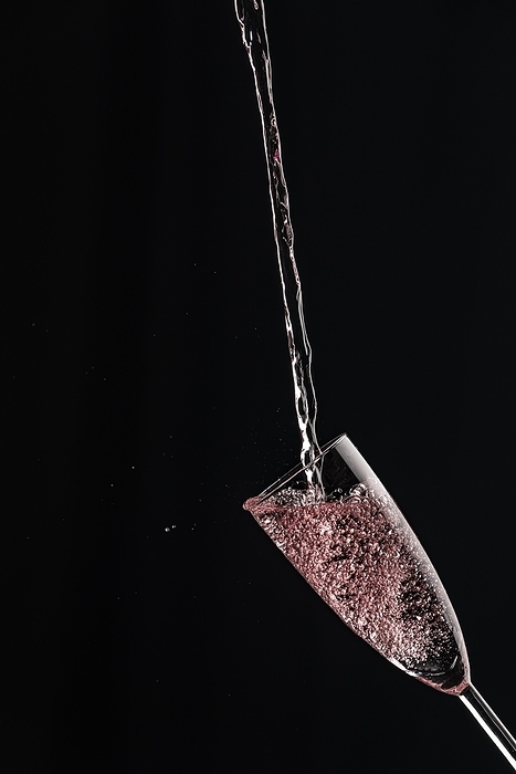 A champagne glass catches rosé sparkling wine against a dark background, by Lucas Seebacher