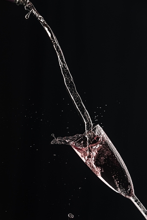 Rosé champagne pours in an arc into a champagne glass on a black background, by Lucas Seebacher