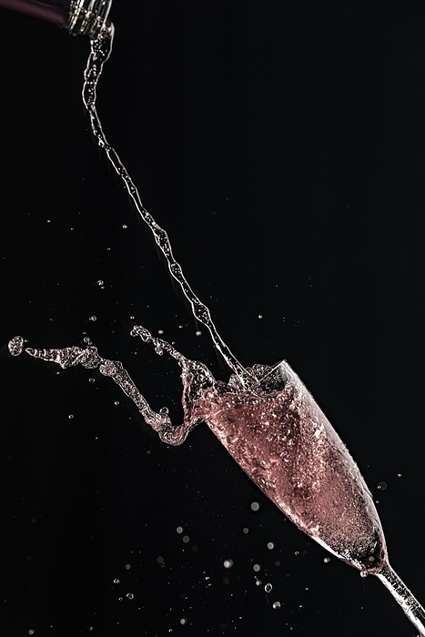 Rosé champagne pours from a bottle into a champagne glass, drops and splashes fly, black background, by Lucas Seebacher